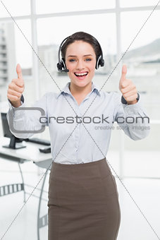 Elegant businesswoman wearing headset while gesturing thumbs up in office