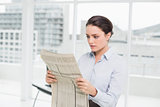 Beautiful businesswoman reading newspaper in office