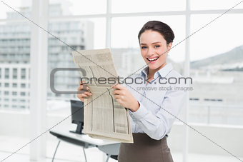 Smiling young businesswoman with newspaper in office