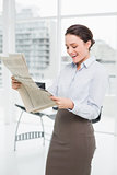 Cheerful businesswoman reading newspaper in a office
