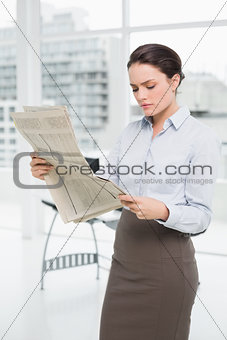 Serious businesswoman reading newspaper in office