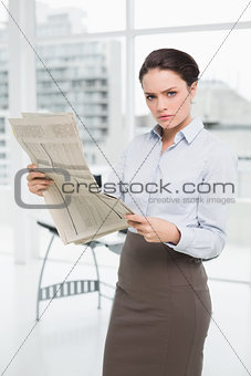 Serious young businesswoman with newspaper in office