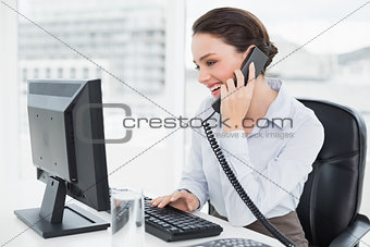 Smiling businesswoman using landline phone and computer in office