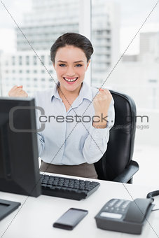 Excited businesswoman clenching fists at office desk