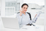 Businesswoman with graphs and laptop gesturing okay sign in office