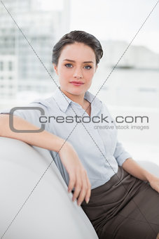 Serious well dressed young woman sitting on sofa