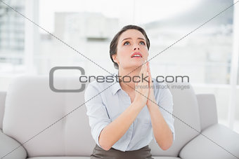 Worried well dressed woman with joined hands looking up