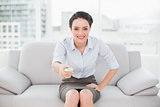 Smiling elegant woman with remote control sitting on sofa