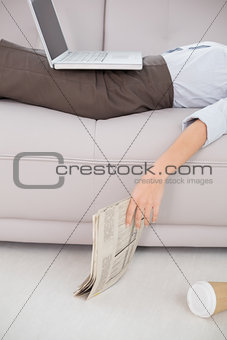 Woman with laptop and news paper lying on sofa
