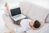 Businesswoman with laptop lying on sofa at home