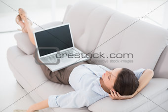 Businesswoman with laptop lying on sofa at home