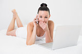 Shocked casual woman using cellphone and laptop in bed