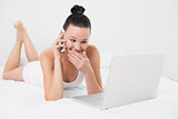 Smiling woman using cellphone and laptop in bed