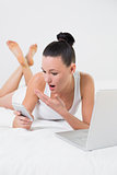 Shocked casual woman with cellphone and laptop