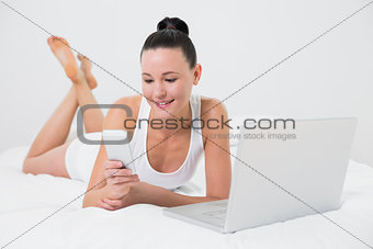 Smiling casual woman using cellphone in bed