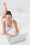 Casual smiling woman using laptop in bed