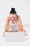 Shocked casual woman using laptop in bed
