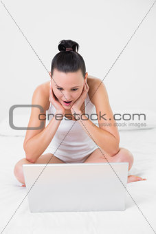 Shocked casual woman using laptop in bed