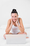 Casual smiling woman with laptop sitting on bed