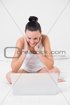 Casual smiling woman looking at laptop in bed