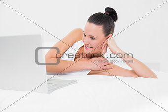 Casual smiling woman using laptop in bed