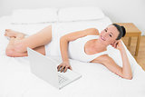 Casual smiling woman with laptop in bed