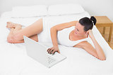 Casual young woman using laptop in bed