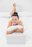Casual smiling woman with laptop in bed