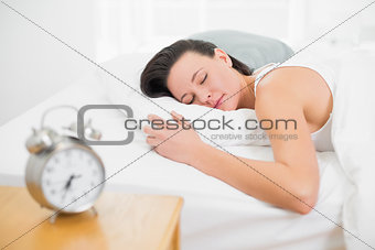 Woman sleeping in bed with alarm clock on bedside table