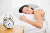 Blurred woman sleeping in bed with alarm clock on bedside table