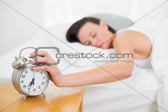 Woman in bed extending hand to alarm clock at home