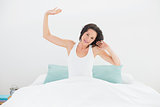 Wmiling woman stretching her arms in bed