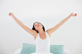 Woman stretching her arms with eyes closed in bed