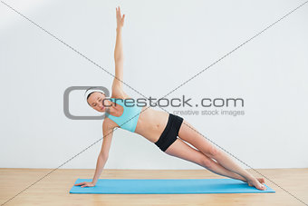 Slim woman doing the side plank yoga pose in fitness studio
