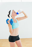 Toned woman with dumbbells drinking water