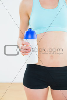 Mid section of a sporty fit woman holding water bottle