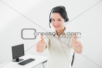 Businesswoman wearing headset and gesturing thumbs up in office