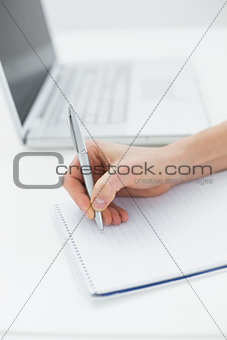 Close up of a hand writing notes by laptop