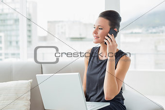 Beautiful well dressed woman using laptop and cellphone on sofa