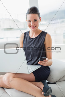 Beautiful well dressed woman using laptop and cellphone on sofa