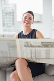 Smiling beautiful businesswoman reading newspaper on sofa