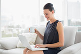 Beautiful well dressed woman using laptop while having coffee on sofa