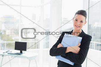 Elegant businesswoman leaning on glass wall with folder