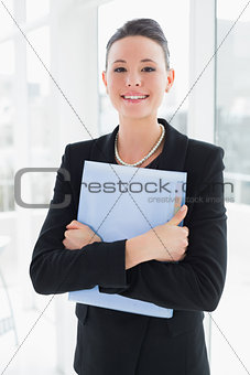 Elegant businesswoman standing against office glass wall with folder