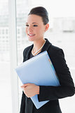 Businesswoman standing against office glass wall with folder