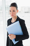 Elegant businesswoman standing against office glass wall with folder