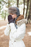 Woman in winter wear sneezing in woods