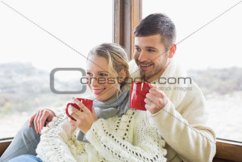Couple in winter wear drinking coffee against window