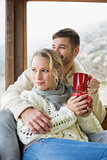 Couple in winter wear with cups looking out through window