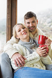 Loving couple in winter wear with cups against window